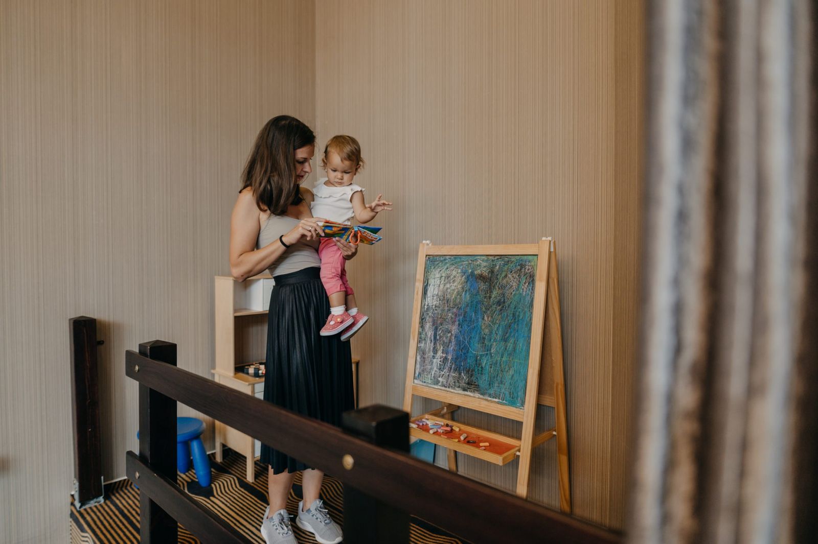 Anya a karján tartja a kisgyereket a játszósarokban