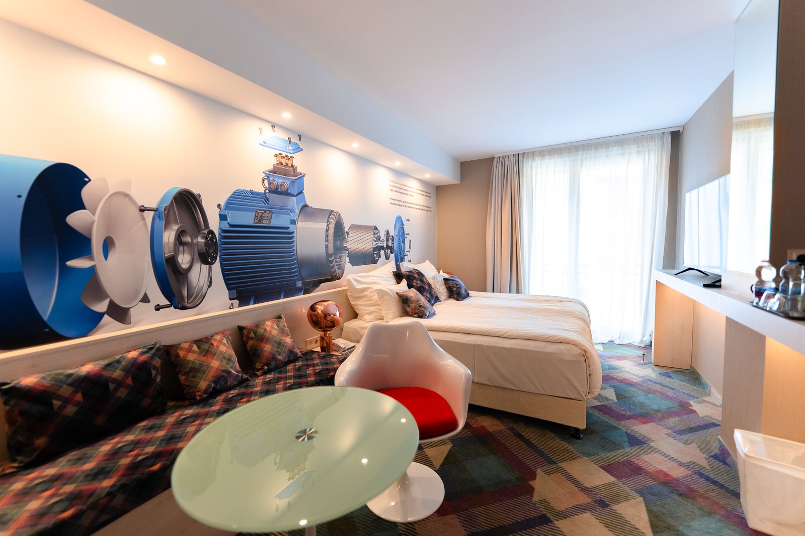 A spacious Science Prémium room with a double bed, a seating area and a wall image of an electric motor